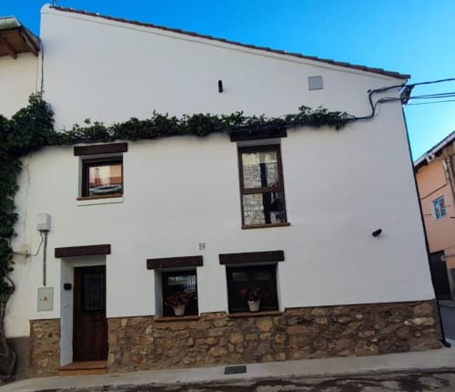 Casa rural El Abuelo en Bronchales: paredes blancas, base de piedra, puertas y ventanas de madera oscura, decorada con hiedra