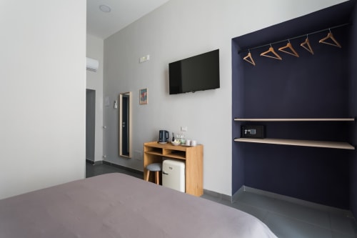Modern bedroom at Darna Rooms Naples with flat-screen TV, wooden desk, dark accent wall with shelving and wooden hangers