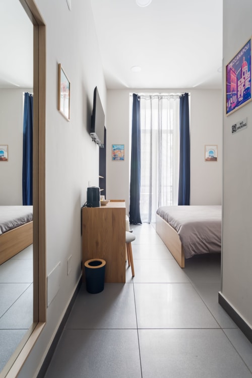 Modern twin bedroom at Darna Rooms Naples with wood furniture, blue curtains, balcony access, and city views