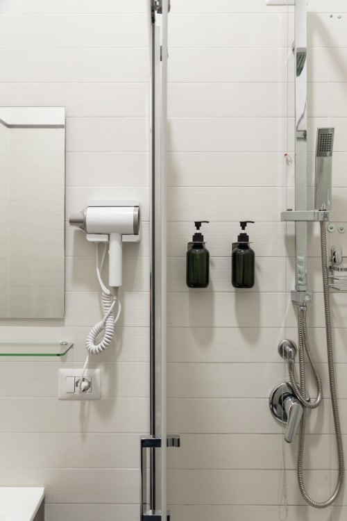 Modern bathroom shower area at Darna Rooms Naples with white tile walls, rainfall showerhead, and green amenity bottles