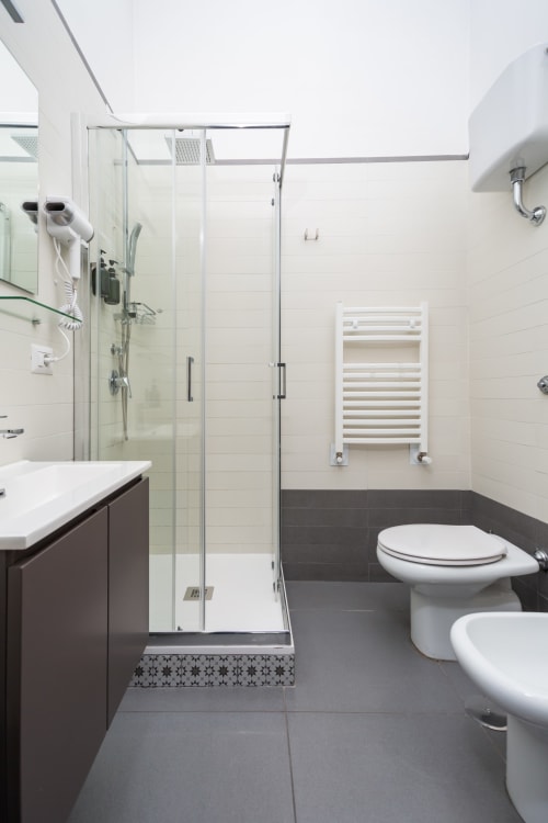 Modern bathroom at Darna Rooms in Naples with dark tile, glass shower, white sink, and heated towel rack