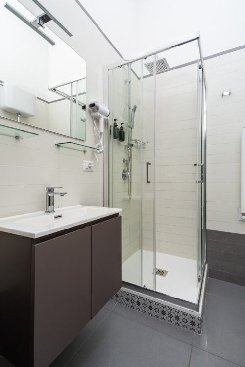 Modern bathroom at Darna Rooms Naples featuring dark vanity, glass shower enclosure, and white tile walls