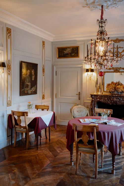 Elegant dining room at Castanea Business & Suites in Merelbeke with crystal chandelier, fireplace, and burgundy tablecloths