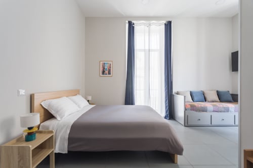 Modern bedroom at Darna Rooms Naples featuring queen bed, balcony with blue curtains, and contemporary furnishings in bright,
