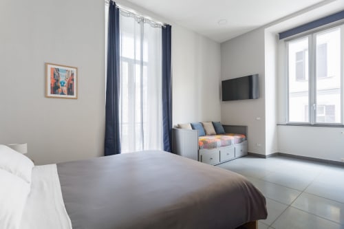 Modern bedroom at Darna Rooms Naples with double bed, flat-screen TV, balcony doors with navy curtains, and contemporary