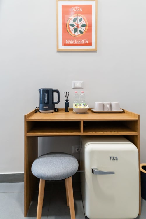 Stylish kitchenette at Darna Rooms Naples with cream minibar, dark kettle, coffee cups, and pizza poster wall art