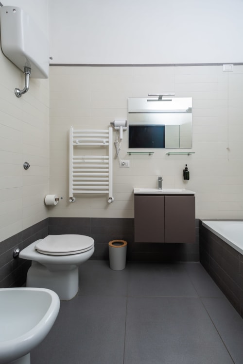 Modern bathroom at Darna Rooms Naples with dark tile floor, white toilet, brown vanity, heated towel rack, and mirror with