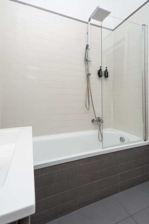 Modern bathroom with rainfall shower, white subway tile walls, dark tile accents, and glass shower enclosure at Darna Rooms