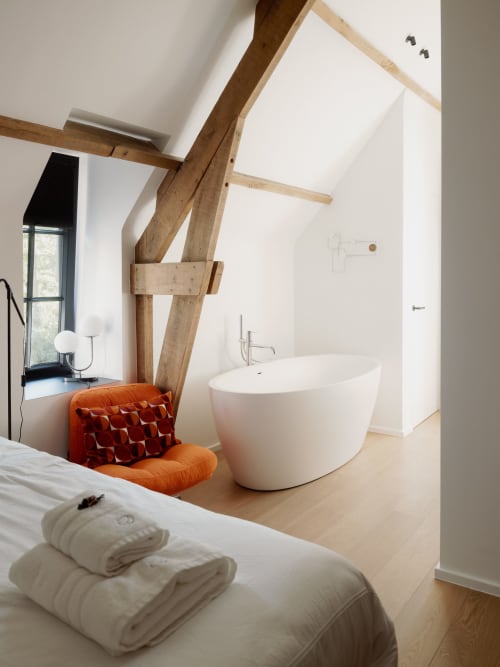 Modern bedroom-bathroom suite at Castanea Business & Suites with exposed wooden beams, white freestanding tub, and orange