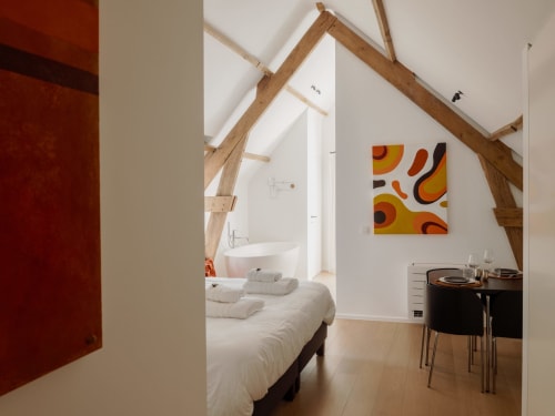 Modern loft-style bedroom at Castanea Business & Suites with exposed wooden beams, white bedding, and colorful abstract