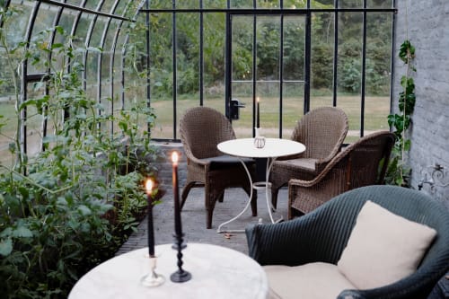 Elegant greenhouse patio at Castanea Business & Suites with wicker chairs, candlelit table, and lush climbing plants in
