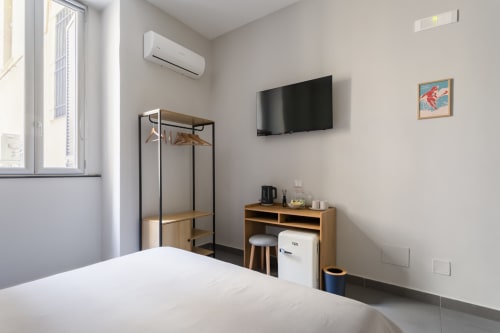 Modern bedroom at Darna Rooms Naples with double bed, flat-screen TV, AC unit, mini desk with refrigerator, and minimalist