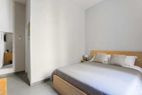 Modern bedroom at Darna Rooms Naples with wooden bed frame, white bedding, and ensuite bathroom
