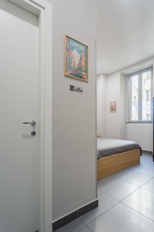 Modern hotel room at Darna Rooms Naples with bed, white walls, colorful travel poster, and no smoking sign