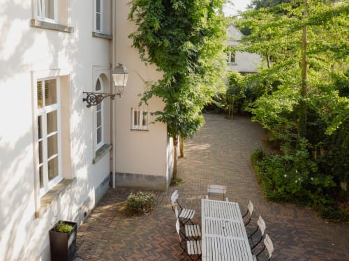 Courtyard patio at Castanea Business & Suites in Merelbeke with dining table, ivy-covered walls, and brick pathways.