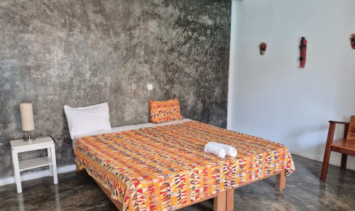 Quarto duplo no Hotel PZero, São Tomé com roupa de cama estampada colorida, almofadas brancas e paredes cinzas texturizadas