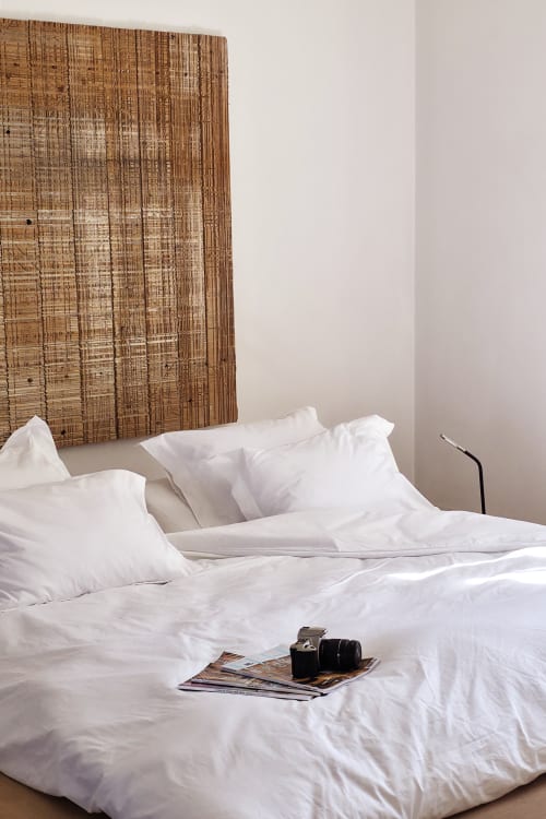 Minimalist bedroom at Castanea Business & Suites with white linens, woven wood headboard, and camera on bed in