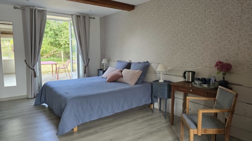 Chambre lumineuse avec literie bleue, bureau en bois et vue sur le jardin au Domaine de la Cour VAUTIER près d'Omaha Beach