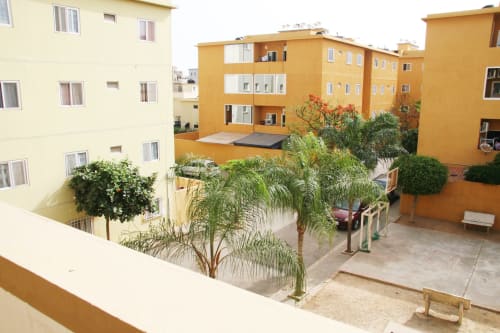 Cour de l'ensemble d'appartements DakarByDays à Almadies, Dakar avec bâtiments jaunes et plantes tropicales