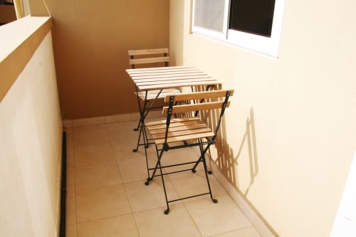 Coin repas compact dans l'appartement DakarByDays avec table pliante et chaises, sol carrelé, fenêtres, quartier des Almadies