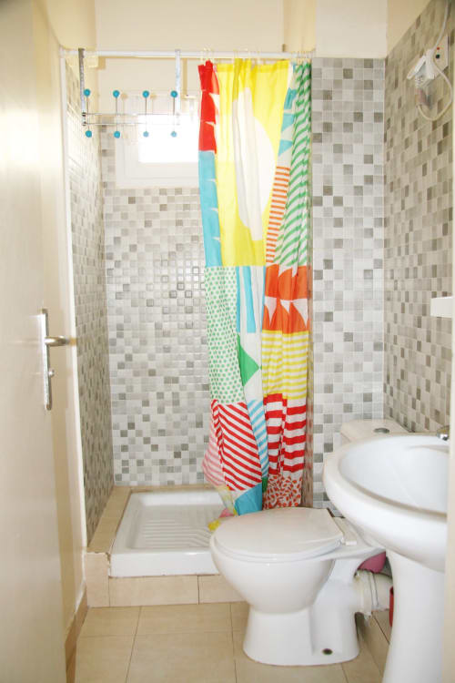 Salle de bain lumineuse de l'appartement DakarByDays avec rideau de douche coloré, toilettes blanches, carrelage à damier et lumière naturelle