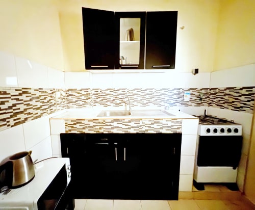 Cuisine moderne dans un appartement de Dakar avec armoires noires, dosseret en mosaïque, cuisinière électrique et miroir encastré