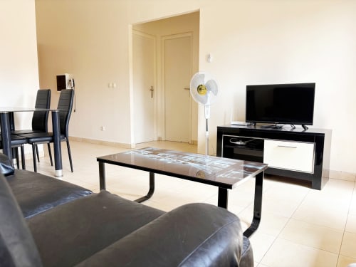 Séjour moderne de l'appartement DakarByDays avec canapé, télévision, ventilateur, coin repas et portes à Almadies, Dakar