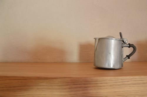 Antico tegame in metallo per senape con manico scuro su tavolo in legno a Villa Rosati, Sanzeno