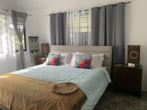 Bedroom at El Litoral Wellness Retreat with beige upholstered bed, colorful pillows, garden view windows, and dark wood