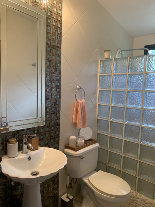 Modern bathroom at El Litoral Wellness Retreat with pedestal sink, toilet, glass block window, mosaic tile accents, and peach