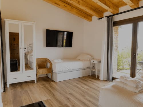 Amplia habitación triple en Hotel Rural Izarbe, Burgos con vigas de madera, acceso al jardín, cama, silla de mimbre y televisión