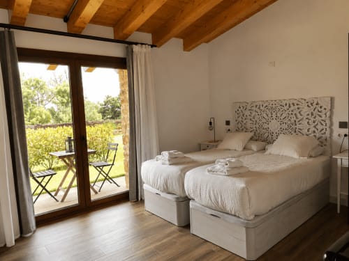 Amplio dormitorio triple en Hotel Rural Izarbe con acceso a jardín, vigas de madera y puertas de patio con vistas a Burgos