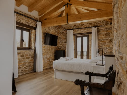 Habitación con vistas a las montañas en Hotel Rural Izarbe, Burgos, con muros de piedra vista, vigas de madera y mobiliario elegante