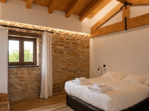 Acogedora habitación doble en Hotel Rural Izarbe de Burgos con muros de piedra, vigas de madera y vistas a la montaña