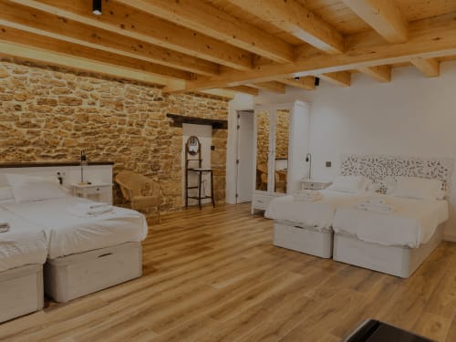 Amplia sala familiar del Hotel Rural Izarbe en Burgos con muros de piedra vista, vigas de madera y múltiples camas blancas