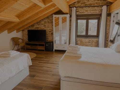 Espaciosa habitación abuhardillada en Hotel Rural Izarbe en Burgos con vigas de madera, muros de piedra, dos camas, TV y vistas a la montaña