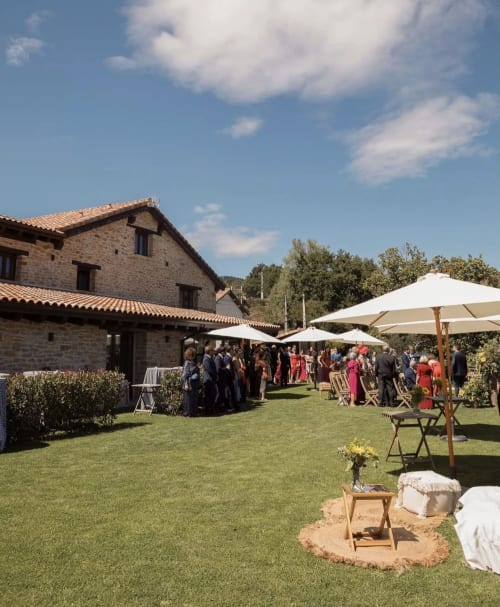 Recepción al aire libre en el jardín del Hotel Rural Izarbe en Burgos con edificio de piedra, sombrillas blancas e invitados en el césped