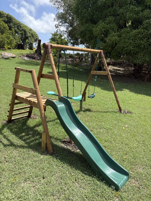 Aire de jeux en bois avec toboggan et balançoires sur la pelouse aménagée de la villa L'Alizé Paradise en Guadeloupe