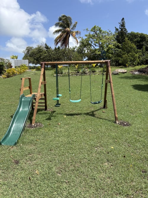 Balançoire en bois avec toboggan sur pelouse verdoyante à la villa L'Alizé Paradise, zone jardin à Grand-Bourg, Guadeloupe