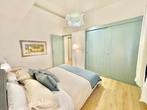 Ampia camera da letto nell'appartamento bolognese con letto queen size, armadi verde salvia, pavimenti in legno e opere d'arte incorniciate.