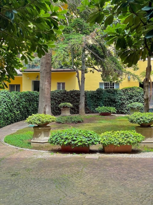 Corte storica di palazzo a Bologna con giardini curati, muri ricoperti d'edera e facciata rinascimentale gialla
