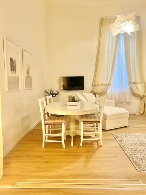 Luminosa sala da soggiorno a Living Palazzi Storici Bologna con tavolo rotondo bianco, sedie color crema e eleganti tende drappate