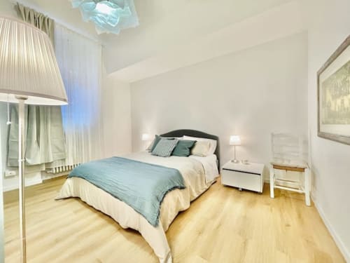 Camera da letto moderna in appartamento bolognese con biancheria blu, struttura nera, pavimenti in legno e arredi bianchi contemporanei