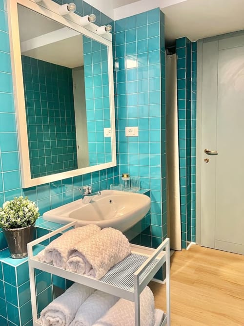 Bagno moderno con piastrelle turchesi, lavabo bianco, specchio incorniciato e portasciugamani a Living Palazzi Storici Bologna