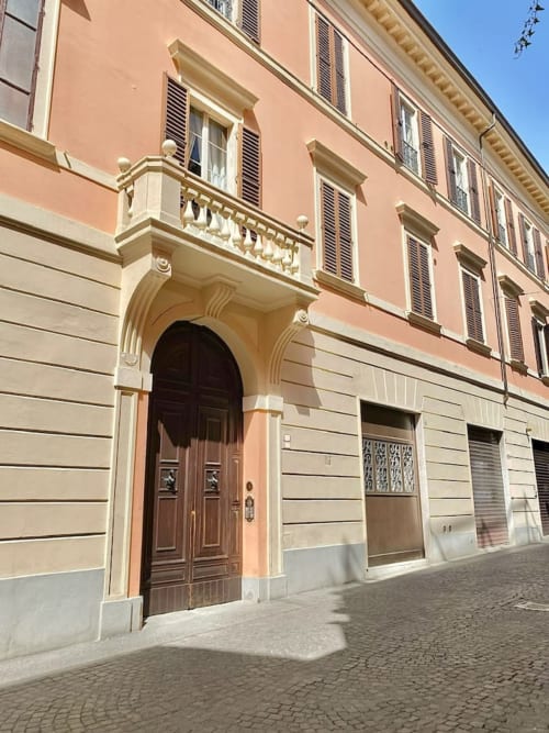 Storica facciata di palazzo a Bologna con muri in terracotta, arco in pietra color crema, porte in legno e finestre con persiane