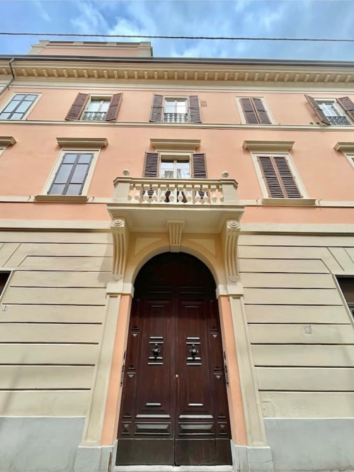 Facciata storica di palazzo a Bologna con tonalità pesca e crema, portone ad arco e persiane in legno