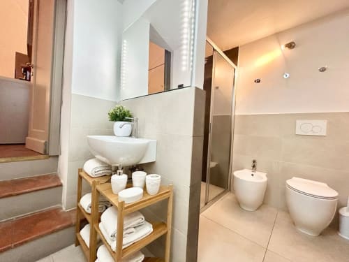 Bagno moderno nell'appartamento di Bologna con specchio illuminato, lavabo bianco, bidet e scaffale in legno