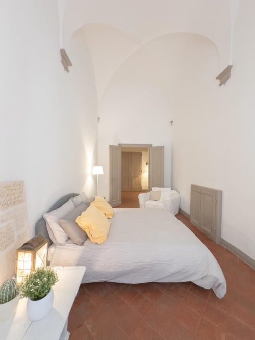 Camera da letto luminosa in palazzo storico bolognese con soffitto a volta, biancheria bianca, pavimenti in legno e piante in vaso