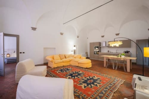 Ampia zona living negli storici Palazzi di Bologna con divano giallo, sedie color crema, tappeto geometrico e moderna cucina
