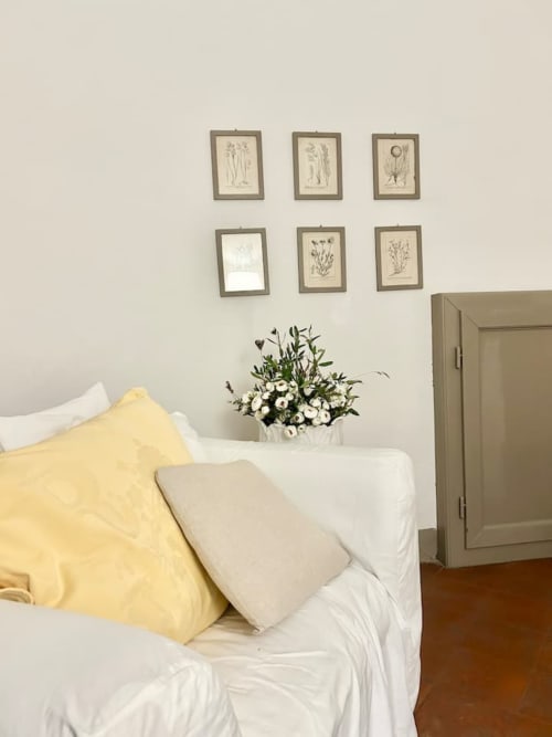 Camera da letto accogliente in storico appartamento bolognese con cuscino giallo, biancheria bianca, arte botanica e fiori freschi